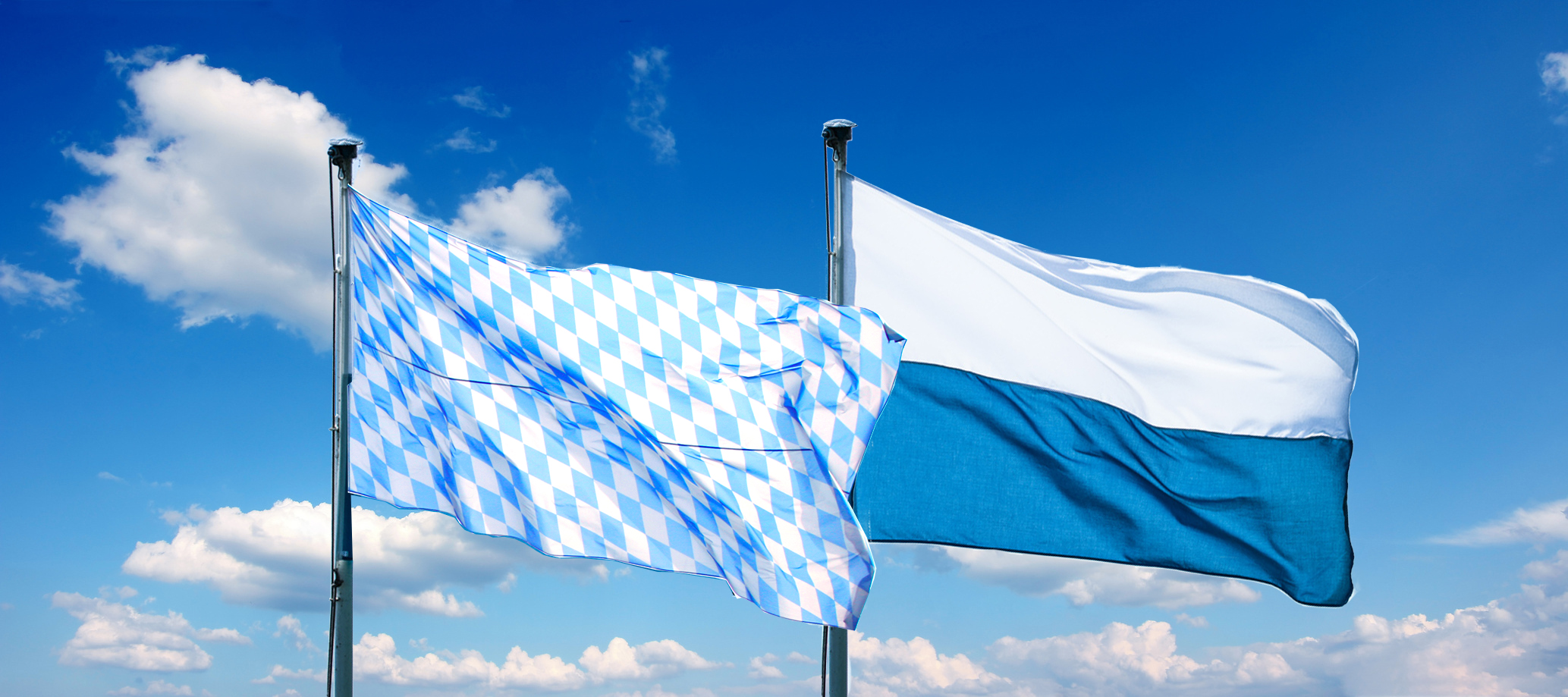 200917_Content_Flaggen Die Rautenflagge (links) und die Streifenflagge (rechts) vor blauem Himmel mit Wolken.